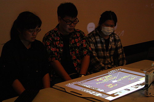 KCG Kyoto Ekimae学校的学生在观看投影在桌面上的KCG Kamogawa学校的文字。