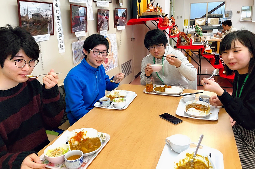 志愿者学生在午餐时相处。菜单是'三三山城Ebi Imo Curry'。